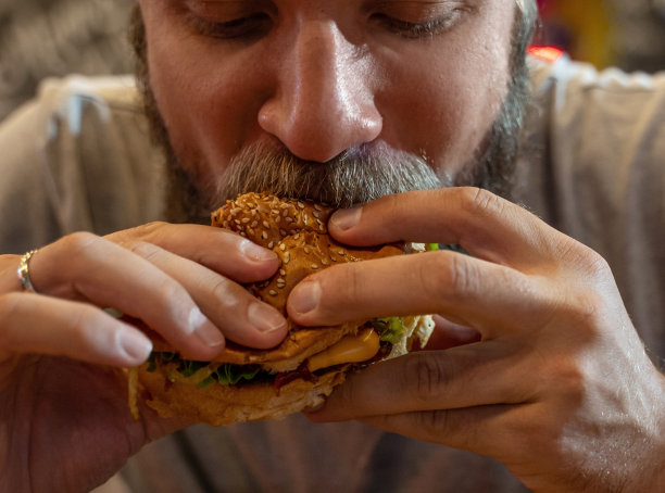 留着胡子的白人中年男子，在咖啡馆或餐厅吃汉堡和快餐。汉堡不是有益的食物。很饿的家伙。饮食的概念。不健康食品的概念，小吃，街头小吃。图片下载