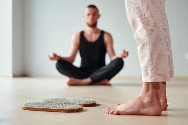 女人的腿站在木制的瑜伽Sadhu板上，用指甲练习和冥想，男人在莲花位置冥想。替代医学穴位按压，恢复力量图片下载