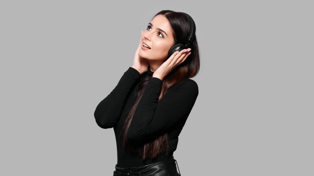 微笑迷人的女子戴着无线耳机听音乐，孤立在灰色的背景上图片下载