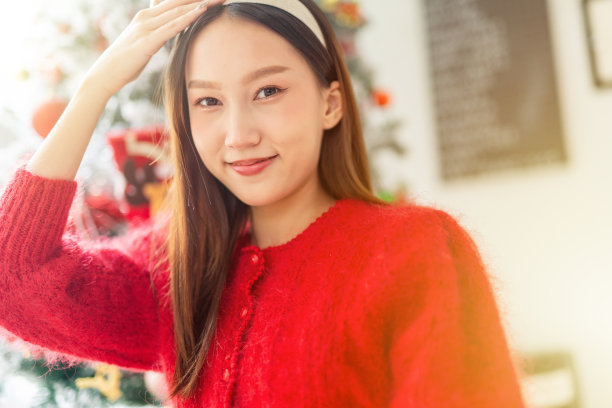 年轻美丽友好的亚洲女性女士，红色长袖毛衣衬衫和可爱的发带摆出不同的样子，在房间里装饰得很漂亮的圣诞树图片下载
