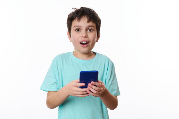 惊讶的可爱少年，拿着手机，看着相机，震惊的脸。哇，很棒的手机应用程序图片下载