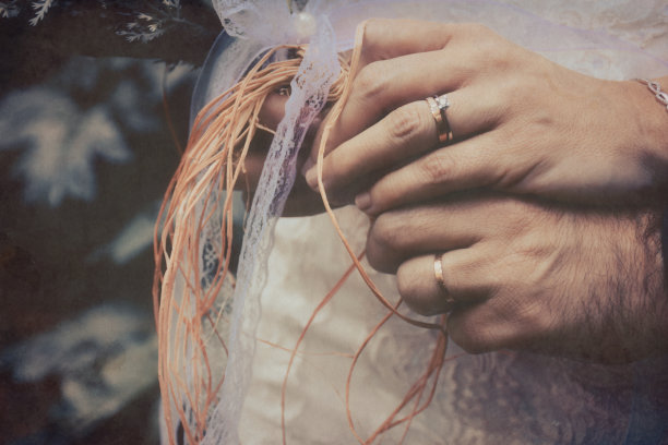 新娘和新郎手持优雅的现代秋季婚礼花束前面的白色婚纱。背景中可以看到新娘和新郎的结婚戒指图片下载