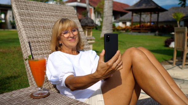 一名中年女子从不同角度拍摄自己的照片和视频，在一家昂贵的海上酒店享受热带假期。未来几年的假期回忆。图片下载