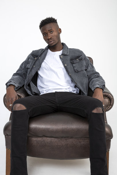一个非洲裔美国人坐在白色背景的皮革扶手椅上。图片下载