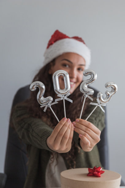 快乐的女商人戴着圣诞帽，玩着数字形状的气球图片下载