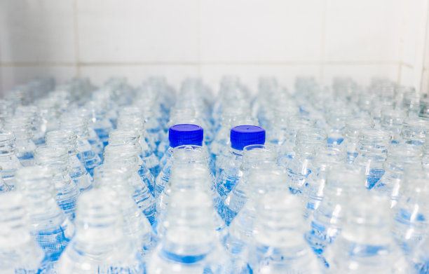 很多水瓶。蓝色瓶盖的瓶子。装瓶厂-水装瓶生产线，用于加工和装瓶饮用水。图片下载