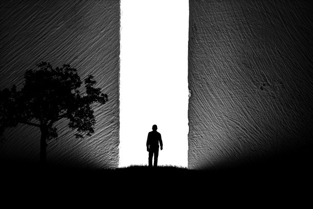 一个男人的剪影在大自然的树旁，走向一个明亮的光在开放的巨大的墙壁。隧道尽头的一束光。成功的概念，自由，选择，开放的心态，冥想。图片下载