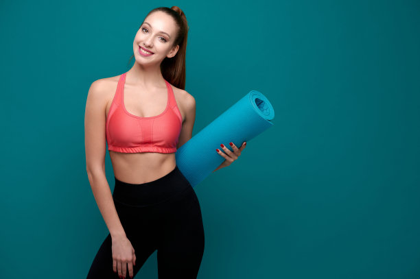 年轻的运动微笑的女人在运动服抱着瑜伽垫在她的手中图片下载