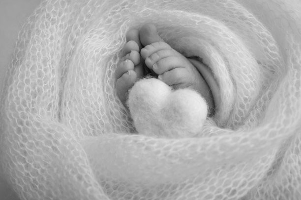 婴儿腿上编织的心脏。柔软的脚，一个新生儿在羊毛毯子。一个新生儿的脚趾，脚跟和脚的特写。微距黑白摄影新生婴儿的小脚。图片下载