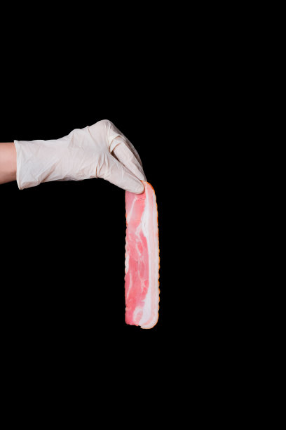 戴着白色防护手套的手拿着黑色背景上长长的、薄薄的、美味的粉红色培根。带有复制空间的垂直食品横幅图片下载