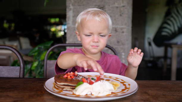 一个可爱又疲惫的白人小孩不想吃端给她的盘子里有水果和奶油的煎饼。那孩子很淘气，揉眼睛。图片下载