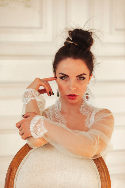 黑发女模特坐在椅子上调情在白色内衣，看着相机，摆姿势在豪华工作室的背景。性感的模特呈现在内衣新系列内衣。复制文本空格图片下载