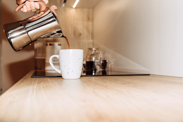 厨房里，一个女人的手把间歇泉咖啡机里的黑咖啡倒进一个白色的杯子里。有选择性的重点图片下载