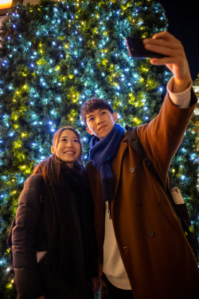 幸福的情侣在圣诞彩灯前自拍图片下载