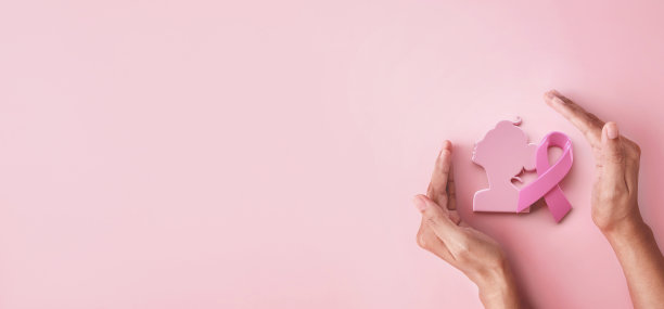 手握保护粉色丝带和女性符号为乳腺癌意识符号为粉红色背景，保护和监测乳腺癌推广十月月运动概念图片下载