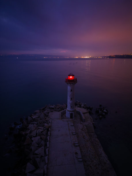 夜晚，海边的灯塔在船只灯光的映衬下发出红光图片下载