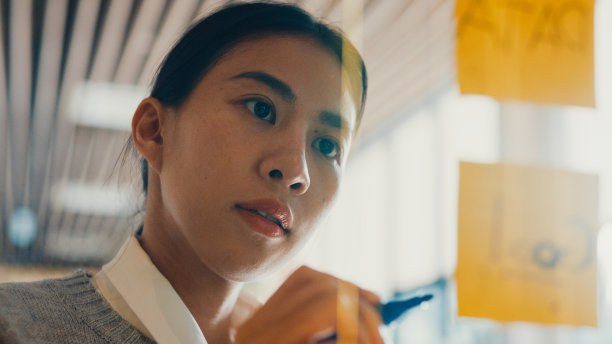 亚洲女孩专注于透明板，书写路线图，在便签纸上规划，在联合工作室的办公室外工作。图片下载