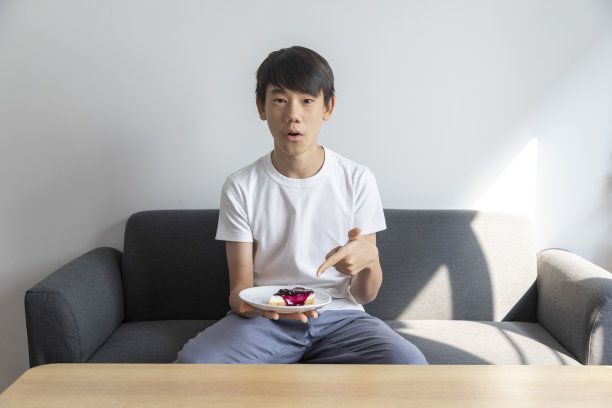 快乐的亚洲少年与蛋糕在盘子里坐在沙发上的房间。图片下载