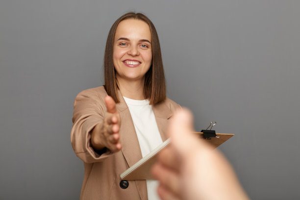 有吸引力的高兴积极棕色头发的女人穿着夹克衫拿着剪贴板的文件，握手，交易，POV，站在灰色背景孤立的肖像。图片下载