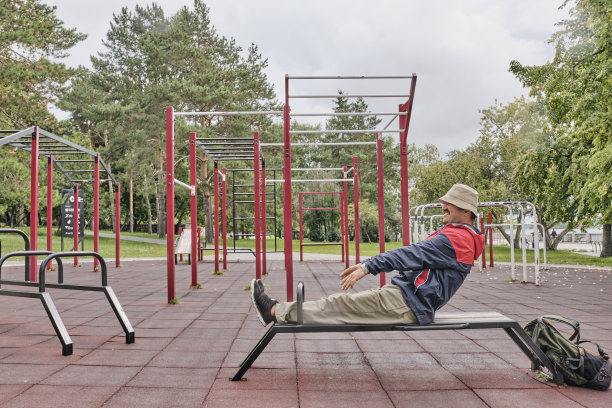 在城市公园的运动设施区，穿着休闲服的亚洲高级男子在长凳上举重。图片下载
