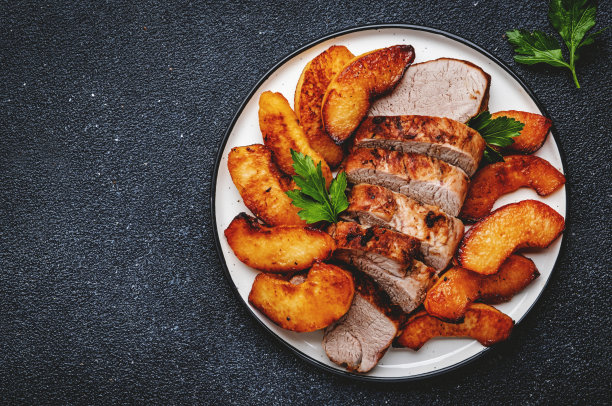 煎猪里脊肉配榅桲或苹果片，盛于盘中。黑色表格背景，俯视图图片下载