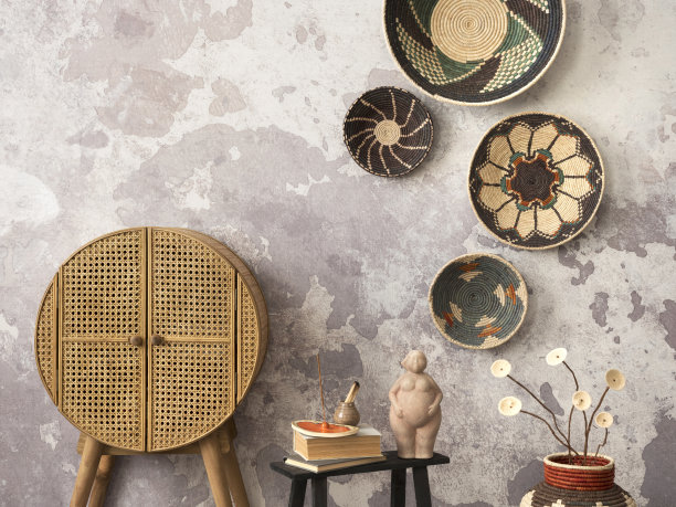 极简主义的民族客厅内饰，色彩缤纷的篮子，藤条餐具柜，黑色凳子，书籍，雕塑，灰色混凝土墙和优雅的个人配饰。家居装饰。模板。图片下载