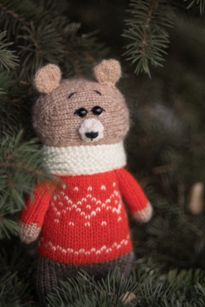 穿着红色圣诞毛衣的小棕熊坐在冷杉树上，选择性地专注着。手工制作的。amigurumi图片下载