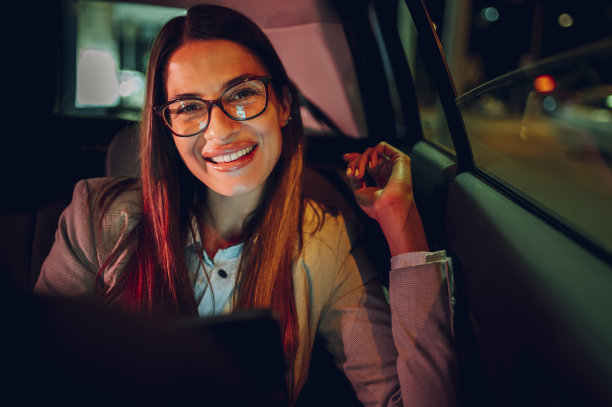 一位商务女性晚上坐在汽车后座上使用智能手机图片下载