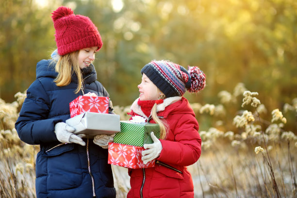 可爱的小女孩在阳光明媚的冬日拿着一堆圣诞礼物。图片下载