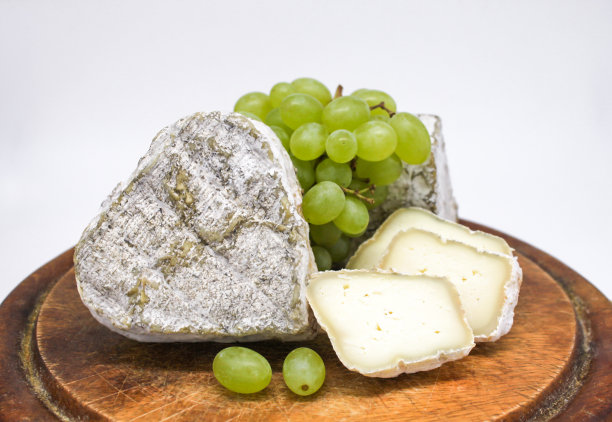 什锦发霉的蓝奶酪、山羊奶放在木砧板上，还有绿葡萄。白色背景图片下载