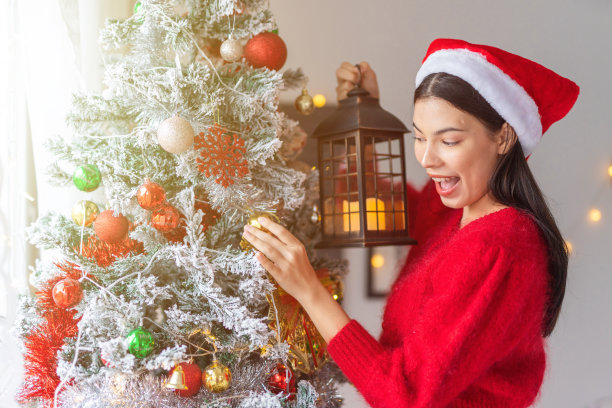 肖像照片的年轻美丽友好的亚洲女性女士与圣诞老人帽手持户外灯笼烛光旁边一个漂亮的装饰圣诞树图片下载