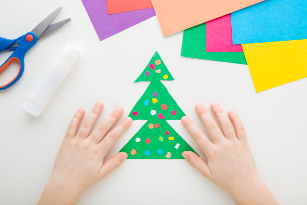 在白色的桌子背景上，小朋友用彩色的纸球制作绿色的圣诞树。制作冬季喜庆的装饰元素。特写镜头。视角镜头。自顶向下视图。图片下载