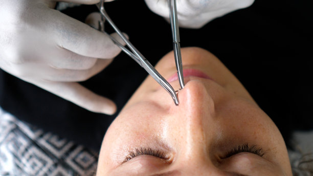 身体穿孔过程。戴着一次性手套的专业穿孔师正确地放置鼻环。该手术是安全的，符合所有无菌标准。图片下载