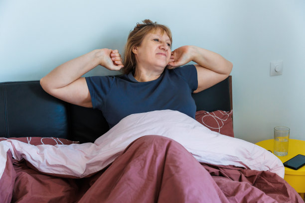 50多岁的老年女性早上醒来，在家里明亮的卧室里伸展坐在床上，中年女性在充足的睡眠后感到快乐和精神饱满，迎接新的一天，早上好图片下载