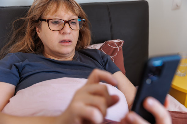 特写照片一个生病的女人在家里，有严重的流鼻涕和感冒，躺在床上盖着毯子，打电话给医生的建议图片下载