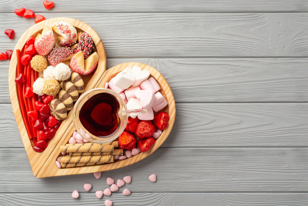 情人节的概念。顶部视图照片的木制心形托盘与糖果巧克力果冻糖果饼干和一杯饮料在灰色的木桌背景与复制空间图片下载