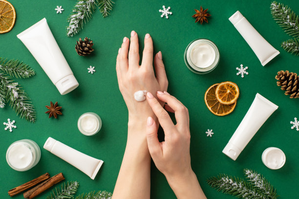 第一人称俯视图照片的年轻女子应用乳液在她的手罐子管杉树树枝肉桂棒松果和干柑橘片在孤立的绿色背景与复制空间图片下载