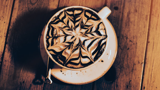 复古的棕色桌子上放着一杯漂亮的拉花图案的拿铁咖啡。图片下载