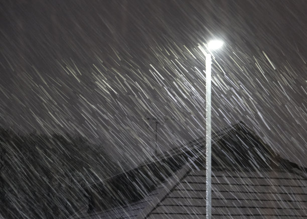 晚上有暴风雪或暴风雪。由路灯照明的屋顶。图片下载