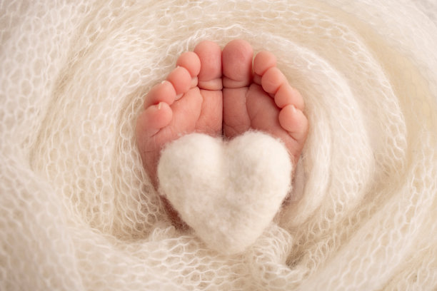 新生儿的小脚。柔软的脚，新生儿在白色羊毛毯子。近距离的脚趾，脚跟和新生儿的脚。婴儿腿上编织的白色心脏。微距摄影。图片下载