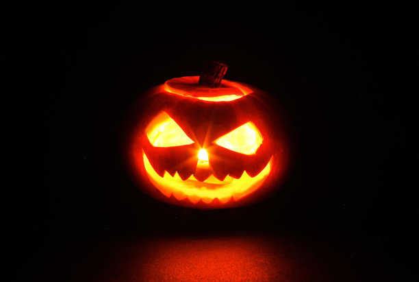 可怕的微笑万圣节杰克灯南瓜头燃烧的蜡烛在黑色背景图片下载