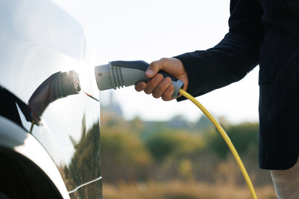 近距离的不认识的男子断开电动汽车从充电站。电动汽车充电。男性手拔下电动汽车电源连接器。绿色能源的概念。图片下载