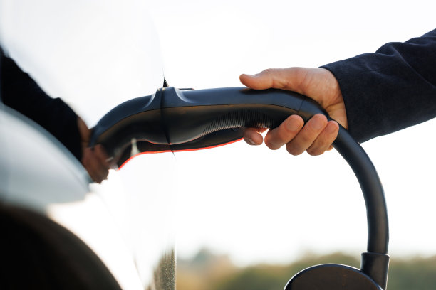 一名不认识的男子将电源线连接到电动汽车上。电动汽车充电电池充电口插在EV现代汽车上。节约生态，替代能源，可持续的未来图片下载