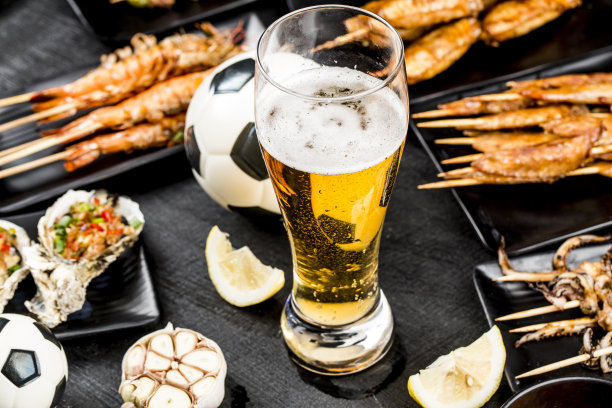 各种烧烤菜肴和啤酒被放置在黑色的木制背景上。看足球比赛，吃烧烤图片下载