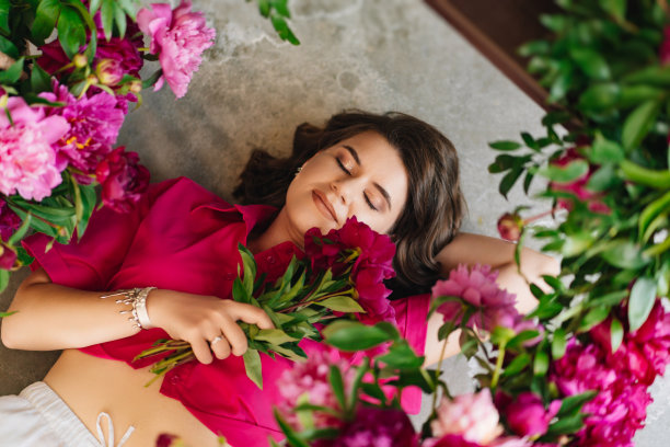 一位迷人的年轻女子，穿着粉红色上衣，地板上有牡丹花。图片下载