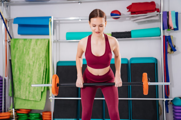 一个美丽苗条的年轻女子在健身房用哑铃做运动。图片下载