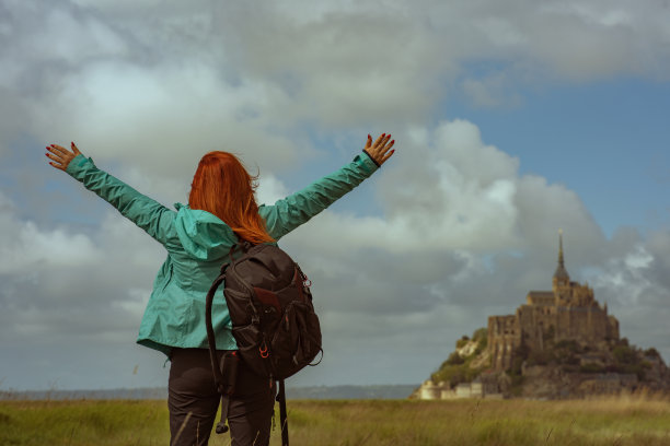 快乐的年轻女子旅行者与背包享受著名的潮汐岛圣米歇尔山的伟大观点图片下载