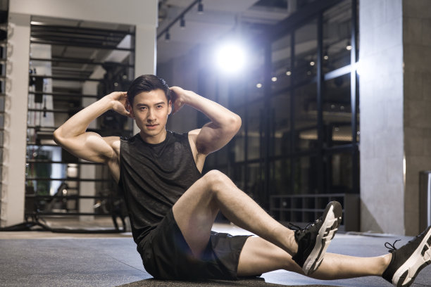 一个年轻男子在健身房地板上做仰卧起坐和侧伸图片下载