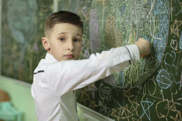 黑板前的男生用粉笔画画。中学年龄。男孩在教室里。图片下载