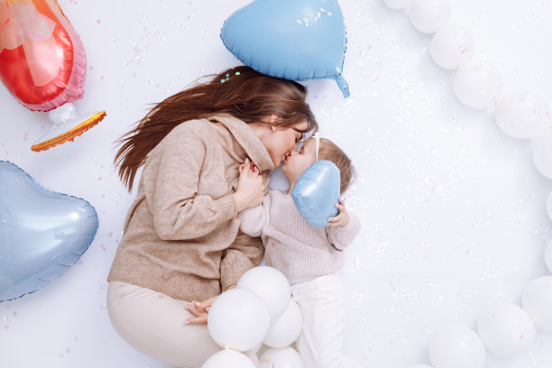 年轻漂亮的妈妈和可爱的小女儿一起躺在彩色的心形气球背景上，拥抱和亲吻。生日，情人节，母亲节图片下载